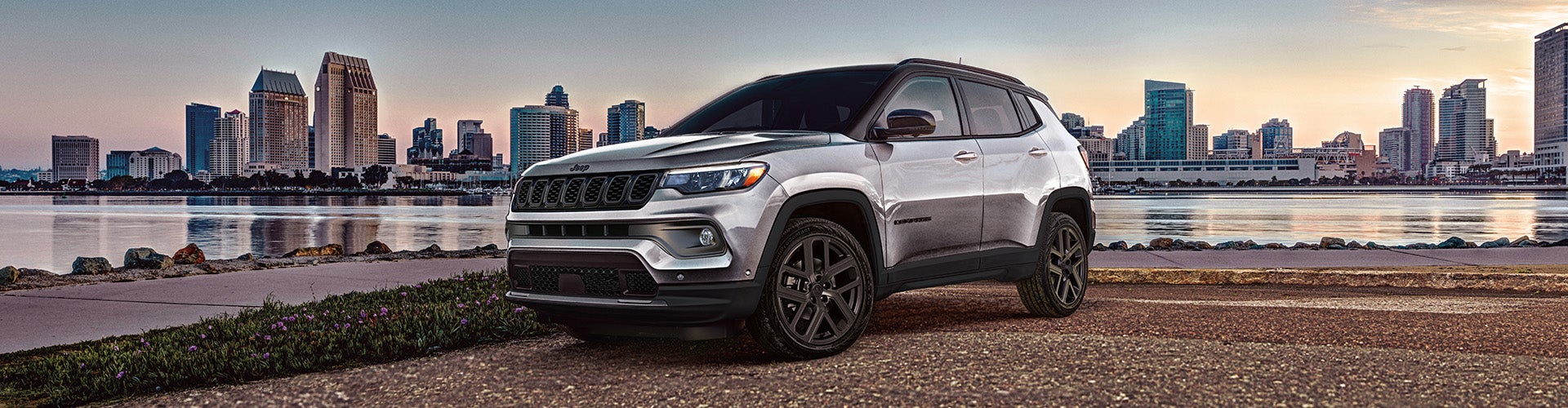 Silver Jeep SUV parked infront of a city in the background
